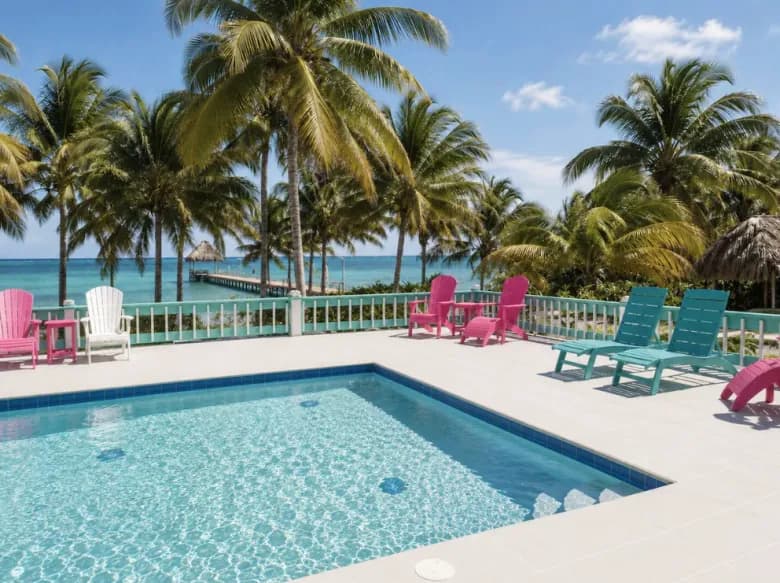 The villa's pool and deck, with pink and turquoise chairs under the palms and the pier beyond