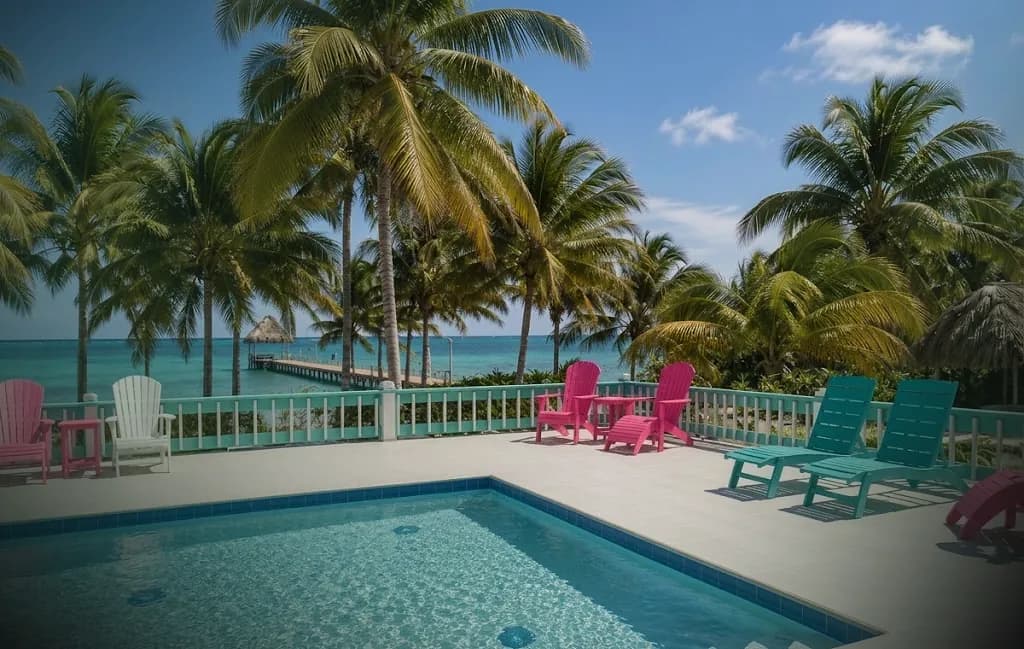 The villa's pool and sun deck under coconut palms, looking out past a wooden pier to the Caribbean