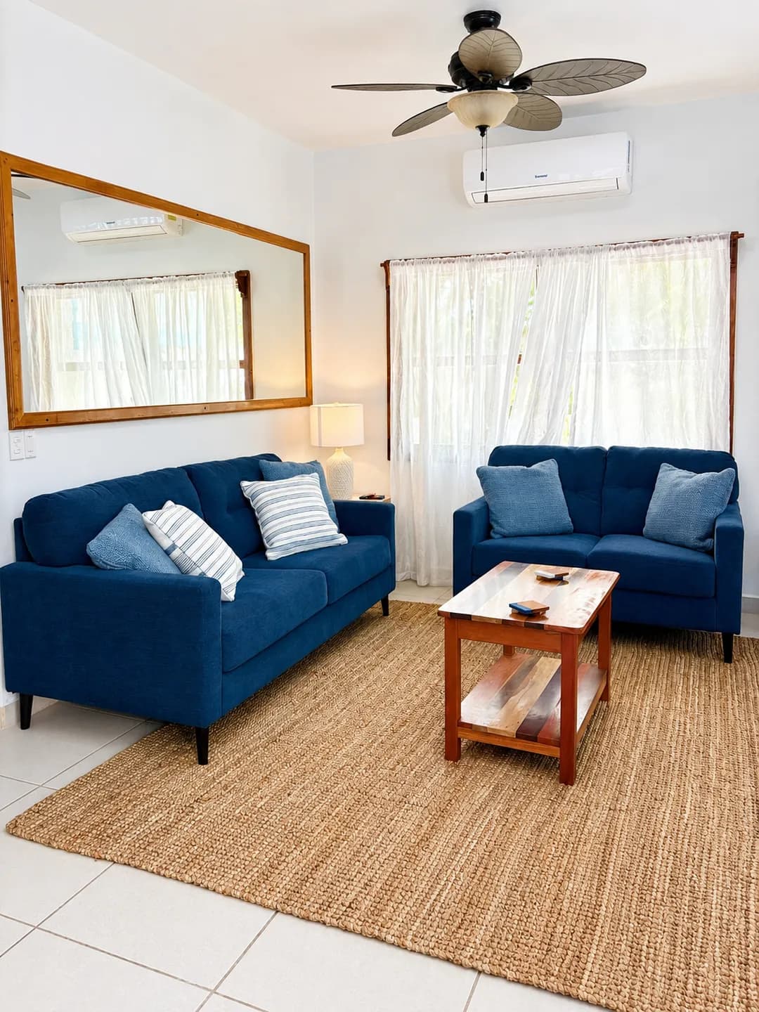 The living room, with navy sofas, a woven rug and a coffee table under a ceiling fan