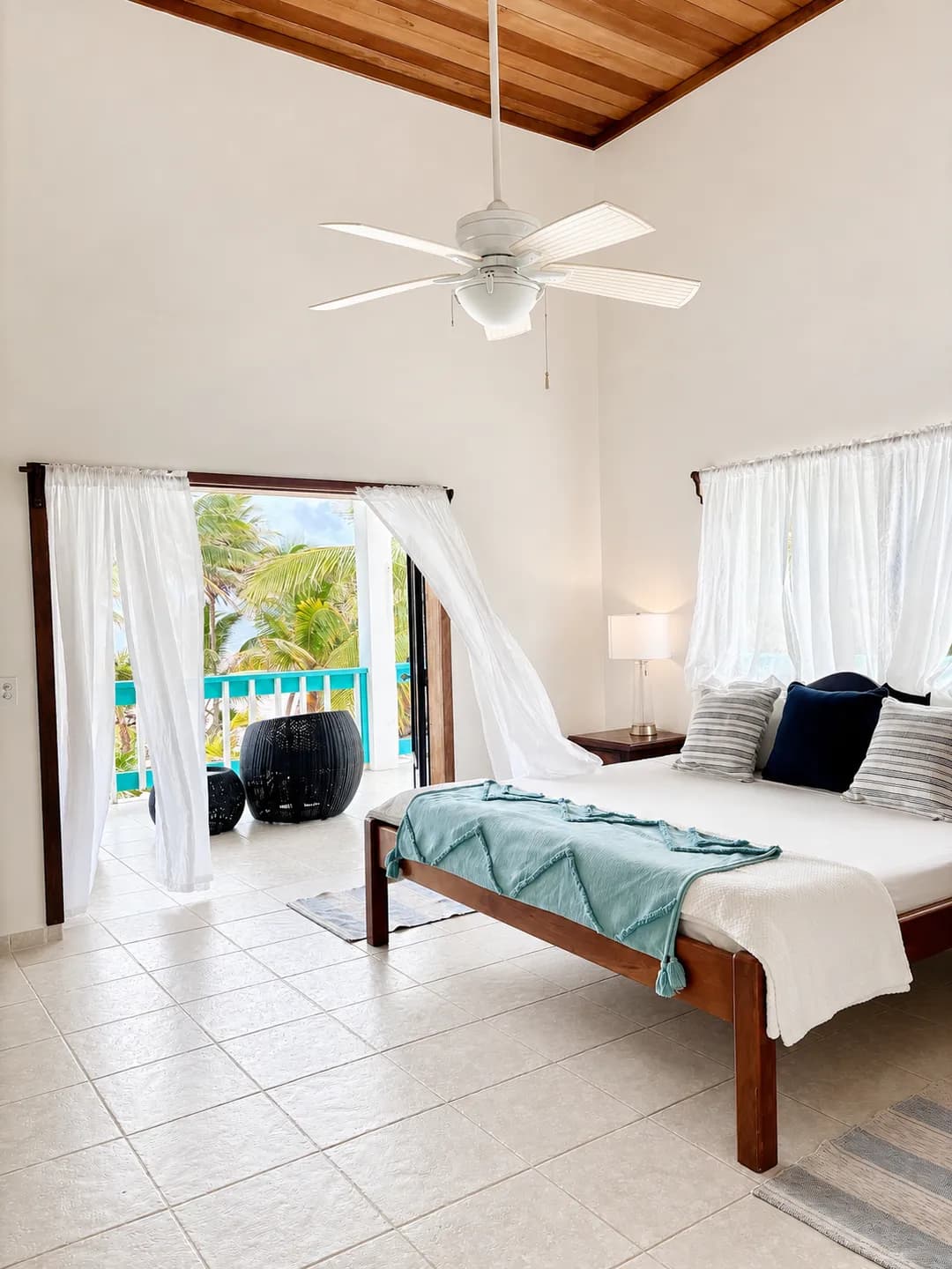 The master bedroom under a wood-beamed ceiling, with sheer curtains open onto a veranda